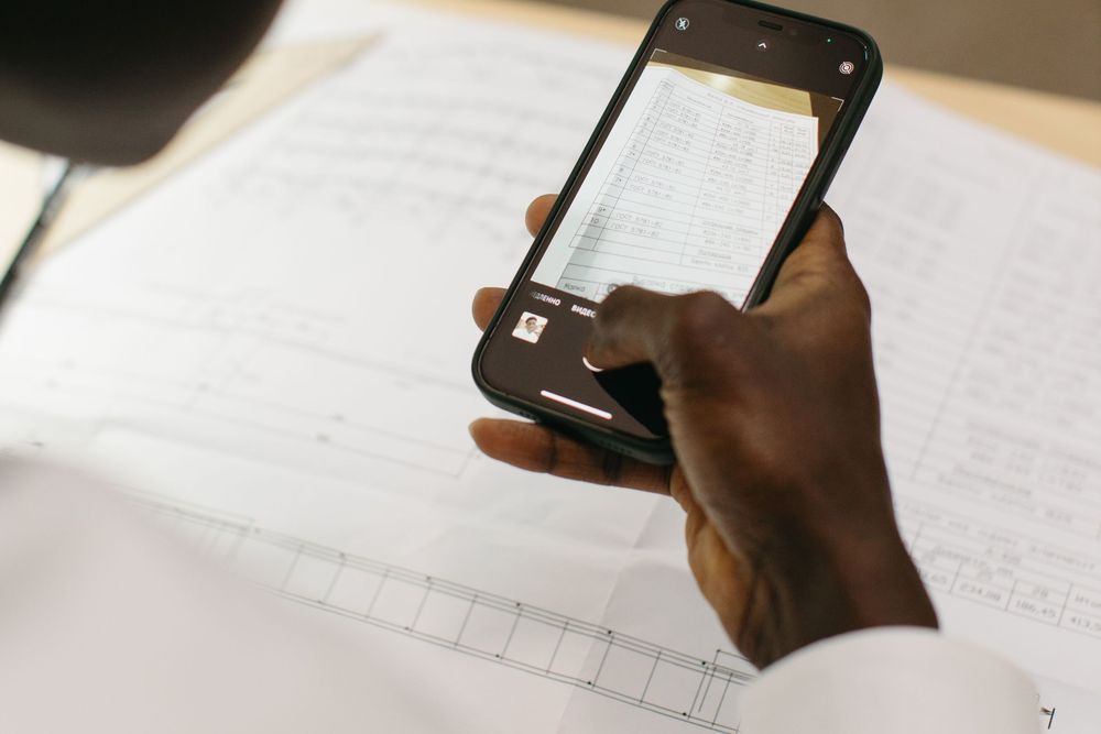 A person holding a smartphone over documents. Photo: Yaroslav Shuraev / Pexels