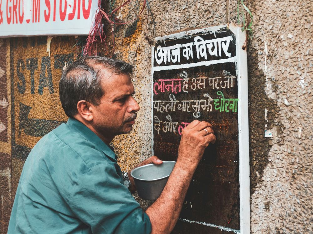 A sign painter lettering a wall board in Chandni Chowk, Delhi. Photo: Akshat Vats / Unsplash